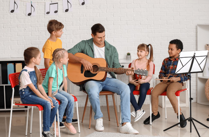 Teacher playing guitar surrounded by kids in music class