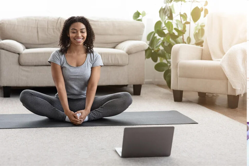 Lady practicing beginners yoga at home in front of her laptop